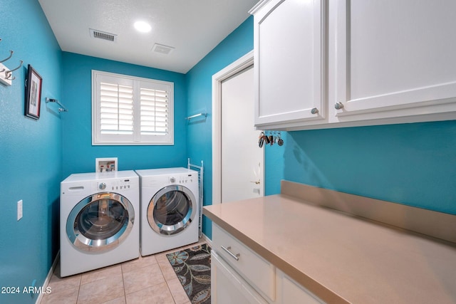 clothes washing area with light tile patterned flooring, cabinets, and washing machine and dryer