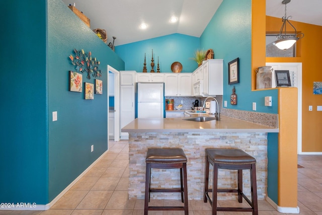 kitchen with white appliances, kitchen peninsula, sink, vaulted ceiling, and white cabinetry