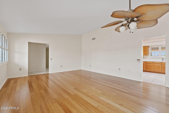 empty room featuring lofted ceiling, a healthy amount of sunlight, light wood-type flooring, and ceiling fan