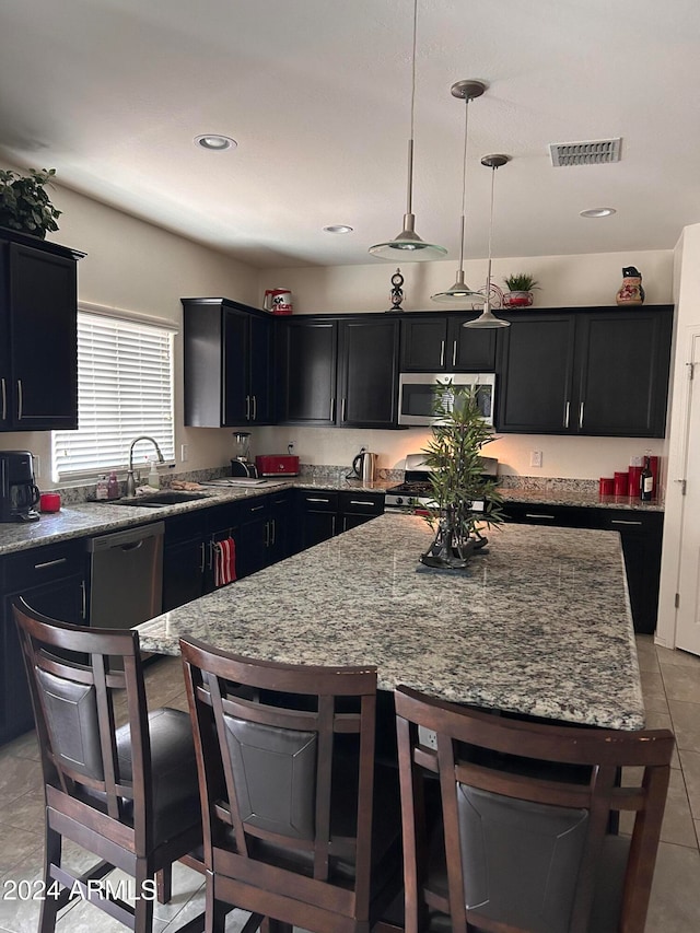 kitchen featuring a kitchen bar, stainless steel appliances, sink, decorative light fixtures, and a center island