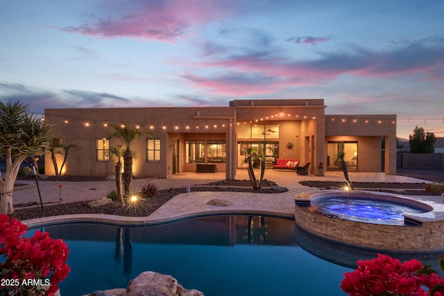 pool at dusk featuring a patio area and an in ground hot tub