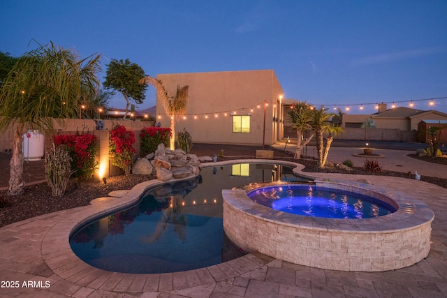 pool at dusk featuring an in ground hot tub and a patio