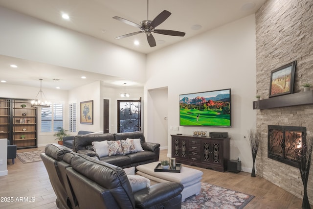 living room featuring a fireplace, a towering ceiling, ceiling fan with notable chandelier, and light hardwood / wood-style floors