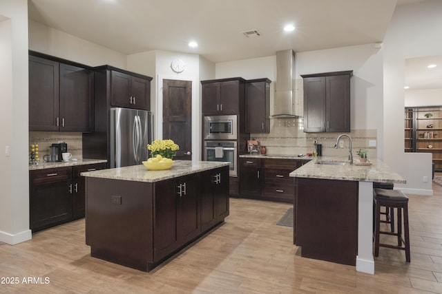 kitchen featuring sink, wall chimney range hood, stainless steel appliances, and dark brown cabinetry