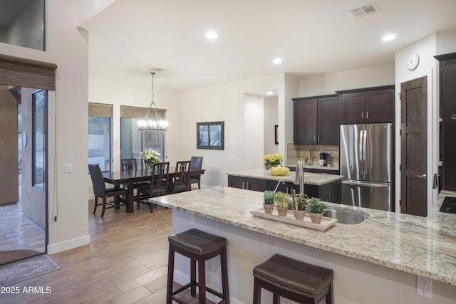 kitchen featuring pendant lighting, light stone countertops, dark brown cabinetry, and stainless steel refrigerator