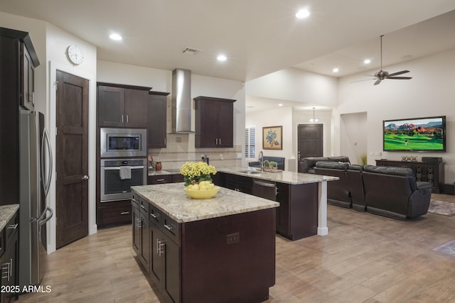 kitchen with wall chimney exhaust hood, stainless steel appliances, sink, light hardwood / wood-style flooring, and a center island