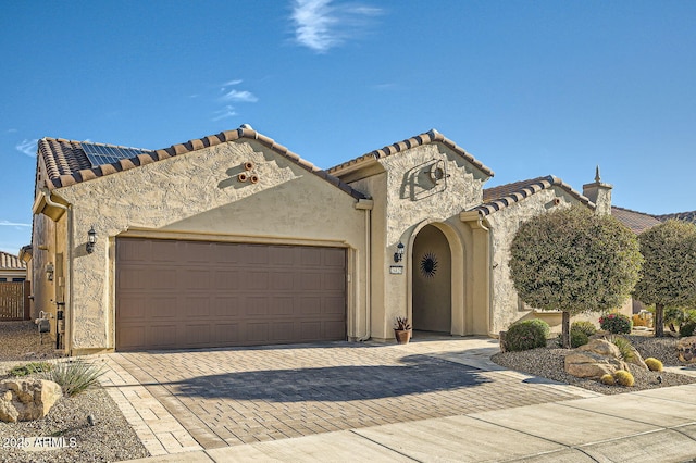 mediterranean / spanish-style home with decorative driveway, a tiled roof, an attached garage, and stucco siding