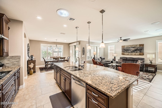 kitchen featuring light stone counters, a sink, stainless steel dishwasher, a center island with sink, and pendant lighting