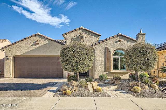 mediterranean / spanish-style house featuring decorative driveway, a tiled roof, an attached garage, and stucco siding