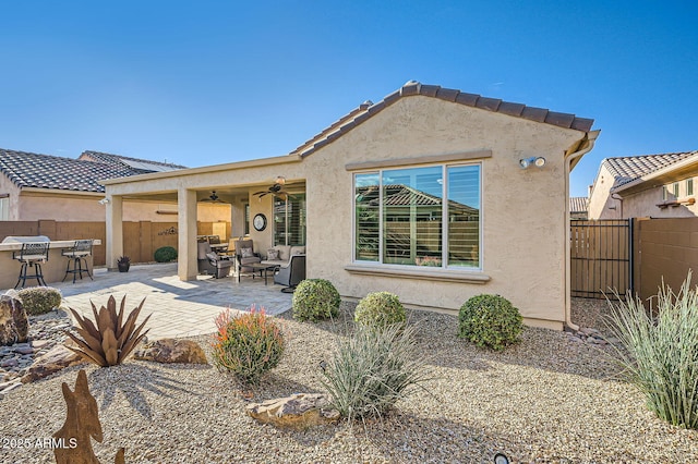 rear view of property featuring a patio, ceiling fan, a tile roof, fence, and stucco siding