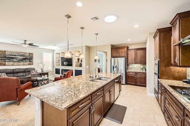 kitchen featuring a kitchen island with sink, a sink, open floor plan, appliances with stainless steel finishes, and pendant lighting