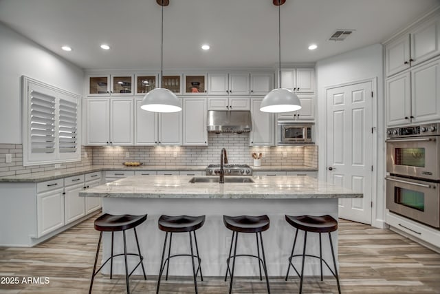 kitchen featuring a kitchen island with sink, appliances with stainless steel finishes, visible vents, white cabinetry, and under cabinet range hood