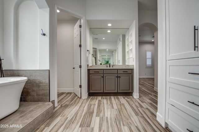 bathroom featuring baseboards, a freestanding bath, vanity, wood finished floors, and recessed lighting