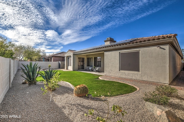 rear view of property featuring a lawn, a fenced backyard, roof mounted solar panels, stucco siding, and a patio