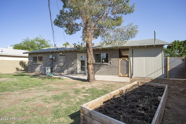 back of house featuring brick siding, a garden, fence, and a yard