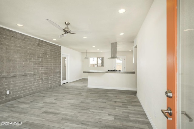 unfurnished living room featuring baseboards, brick wall, wood finished floors, and recessed lighting