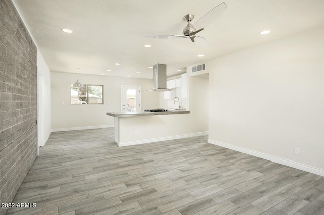 unfurnished living room with ceiling fan, light wood-style flooring, a sink, and visible vents