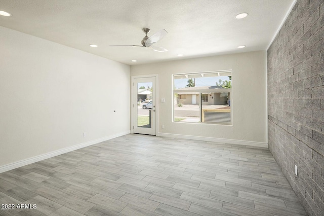 unfurnished room with a ceiling fan, light wood-type flooring, baseboards, and brick wall