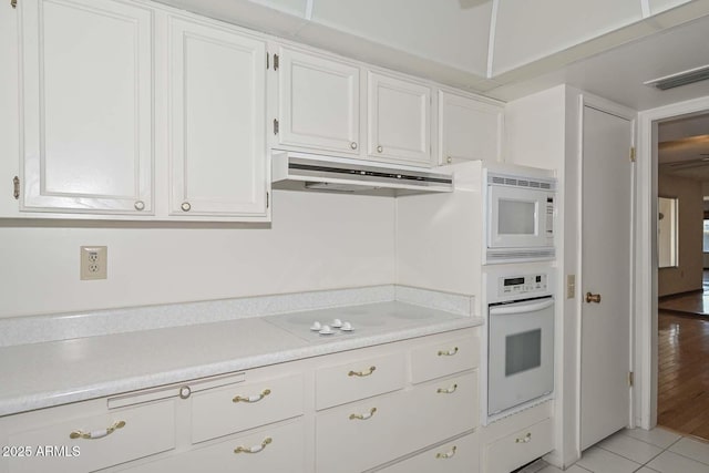 kitchen with light tile patterned floors, under cabinet range hood, white appliances, white cabinetry, and light countertops