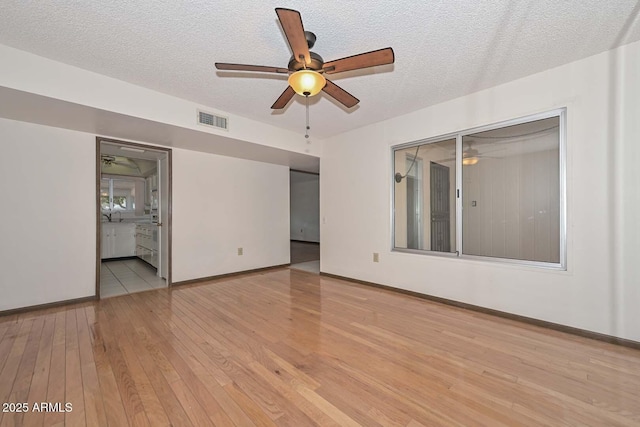 unfurnished room with a textured ceiling, light wood-style flooring, visible vents, and baseboards