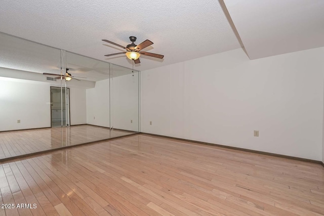 spare room featuring a textured ceiling, ceiling fan, light wood-type flooring, and baseboards