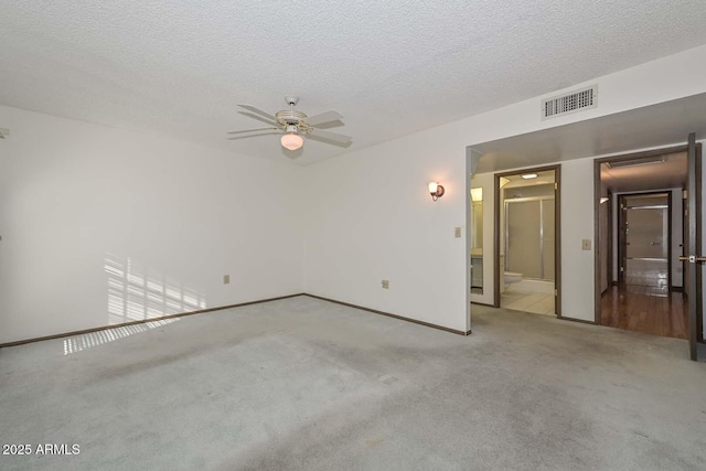 carpeted empty room featuring a ceiling fan, visible vents, a textured ceiling, and baseboards