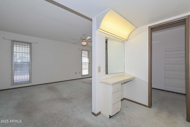 interior space with light carpet, a textured ceiling, a ceiling fan, and baseboards