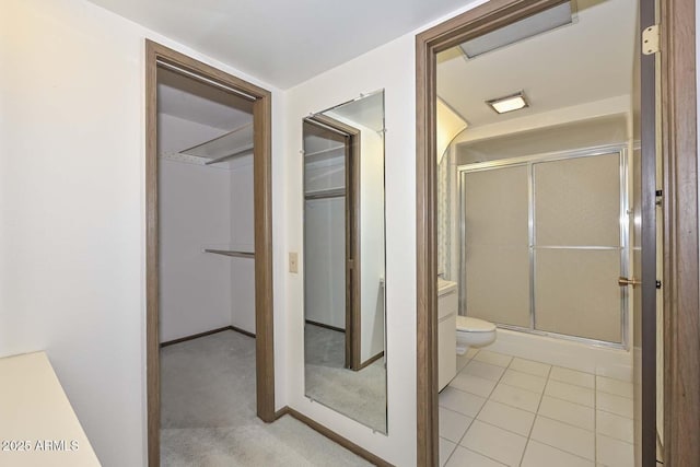 full bathroom with a spacious closet, a shower stall, toilet, and tile patterned floors