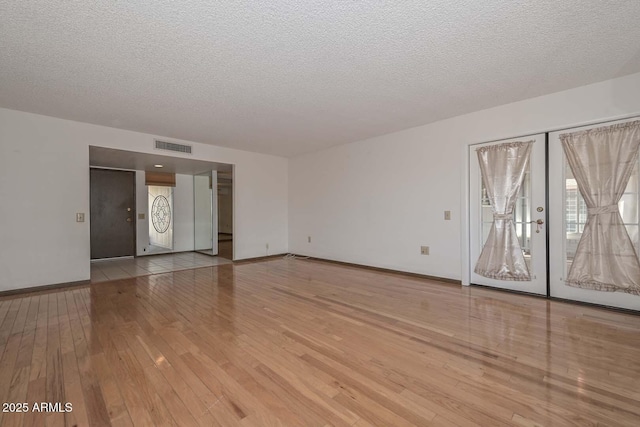 unfurnished room with a textured ceiling, visible vents, and hardwood / wood-style floors