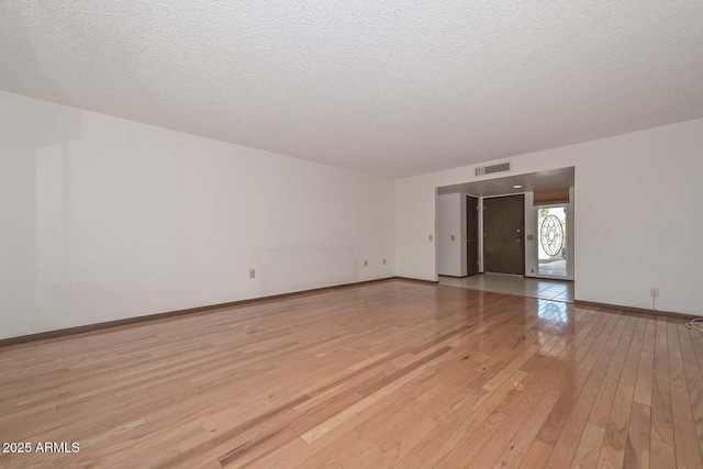 unfurnished room featuring a textured ceiling, light wood-style flooring, visible vents, and baseboards