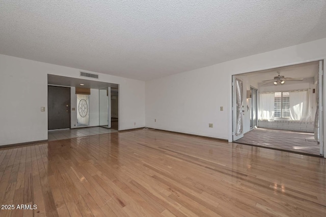 unfurnished living room with visible vents, a textured ceiling, baseboards, and wood finished floors