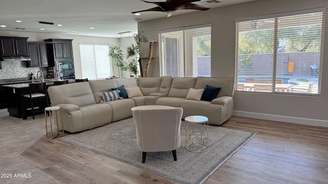 living room with ceiling fan, sink, and light wood-type flooring