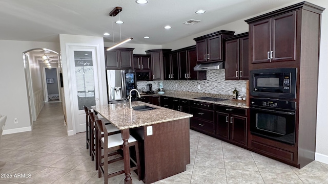 kitchen with an island with sink, sink, decorative backsplash, black appliances, and light stone countertops