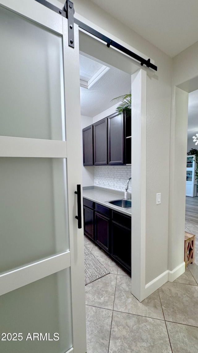 kitchen with light tile patterned flooring, sink, backsplash, a barn door, and dark brown cabinets