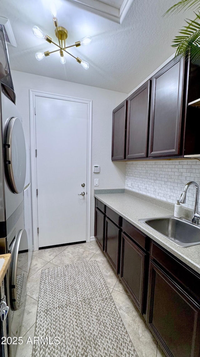 laundry room with cabinets, stacked washer and clothes dryer, sink, and a textured ceiling