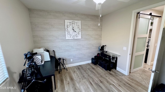 office area featuring ceiling fan, a barn door, light hardwood / wood-style floors, and wood walls