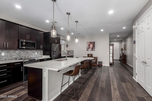 kitchen with dark wood-style floors, stainless steel appliances, a kitchen island with sink, a sink, and a kitchen bar