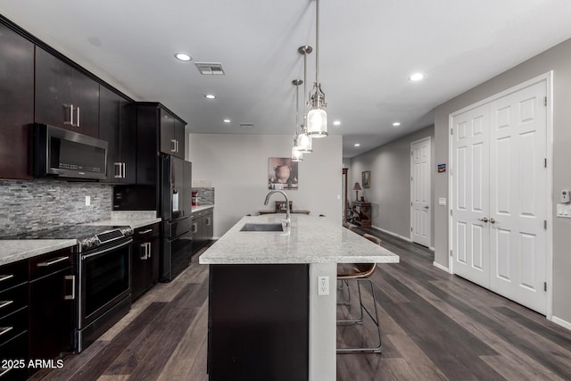 kitchen with a center island with sink, decorative backsplash, appliances with stainless steel finishes, dark wood-type flooring, and a sink