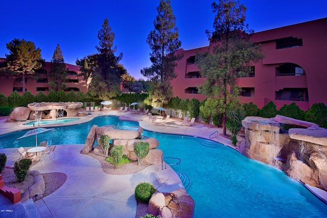 pool at dusk with a hot tub, pool water feature, and a patio area