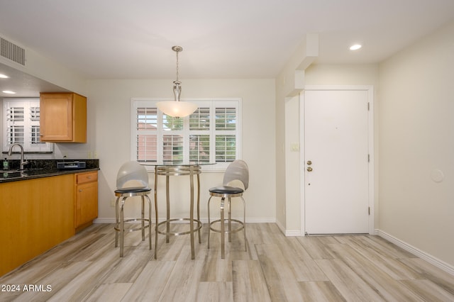 kitchen featuring light hardwood / wood-style flooring, a breakfast bar area, pendant lighting, and sink