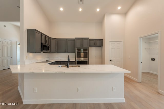 14771 W Columbus Ave, Goodyear, AZ 85395 - kitchen featuring stainless steel appliances, a towering ceiling, a peninsula, light stone countertops, and a sink