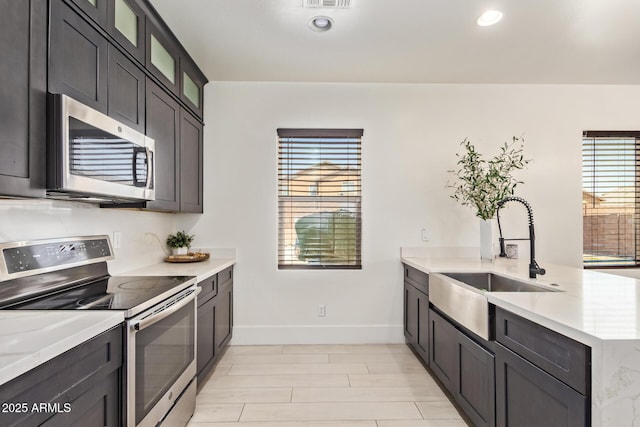 25218 W Carson Ct, Buckeye, AZ 85326 - kitchen featuring stainless steel appliances, a sink, a peninsula, baseboards, and glass insert cabinets