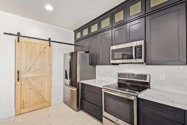 25218 W Carson Ct, Buckeye, AZ 85326 - kitchen with stainless steel appliances, light wood finished floors, light stone counters, a barn door, and glass insert cabinets