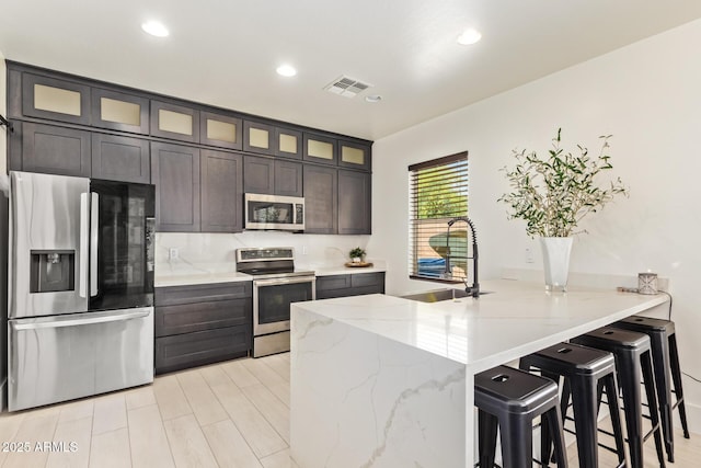 25218 W Carson Ct, Buckeye, AZ 85326 - kitchen featuring stainless steel appliances, a sink, a peninsula, glass insert cabinets, and a kitchen breakfast bar