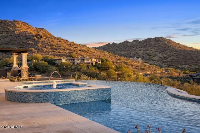 pool at dusk with pool water feature and a mountain view