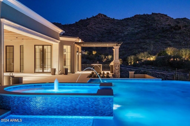 pool at night featuring a patio, a mountain view, and pool water feature