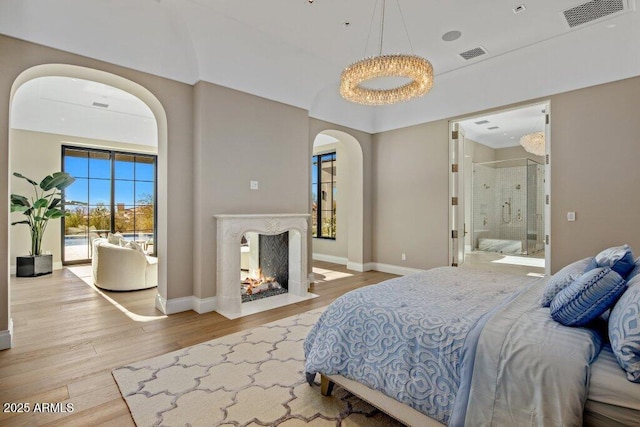 bedroom with access to exterior, ensuite bath, light wood-type flooring, and a multi sided fireplace