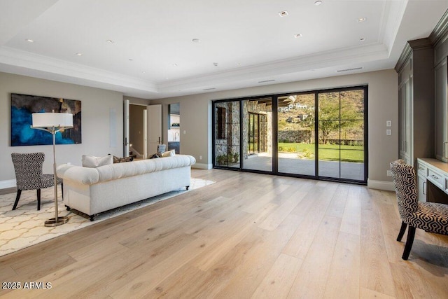 living room featuring a tray ceiling, ornamental molding, and light wood-type flooring