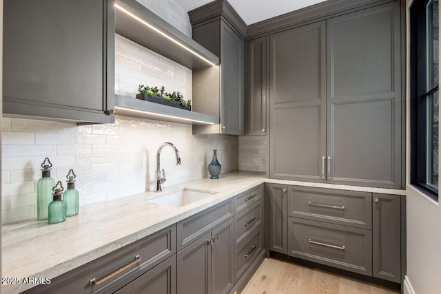 kitchen featuring sink, gray cabinetry, light stone counters, tasteful backsplash, and light hardwood / wood-style floors