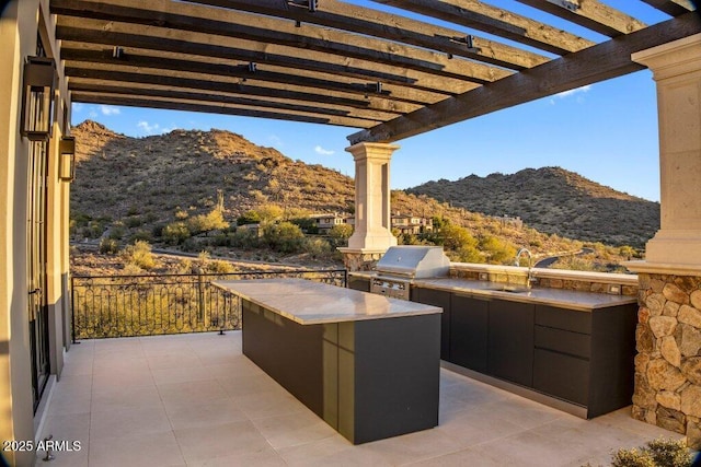 view of patio featuring an outdoor kitchen, sink, grilling area, a pergola, and a mountain view